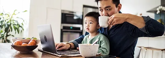 一位父亲坐在儿子的腿上，一边喝咖啡一边查看笔记本电脑.